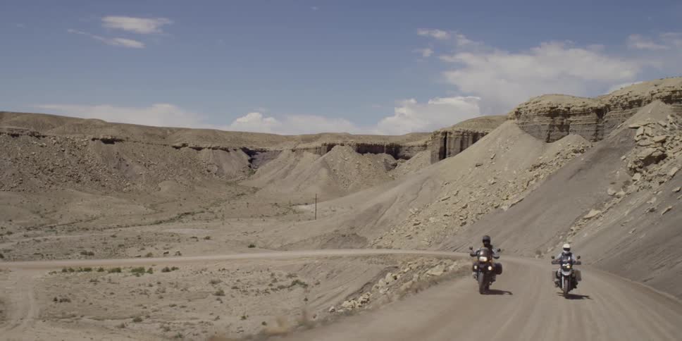 Two people riding motorcycles on a desolate dirt road