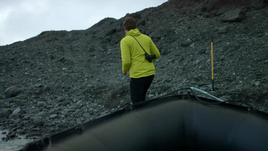 A man climbs out of a rubber dinghy and walks up a hill