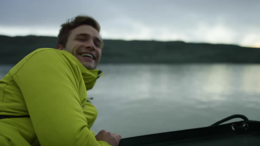 A man in a boat leans over the edge and looks at the water and laughs