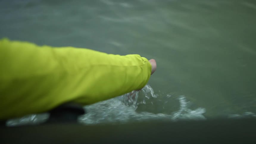 A person runs their hand through the water on the moving boat