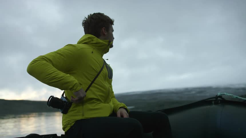 Young man wearing yellow jacket ride a boat on a river uses a camera