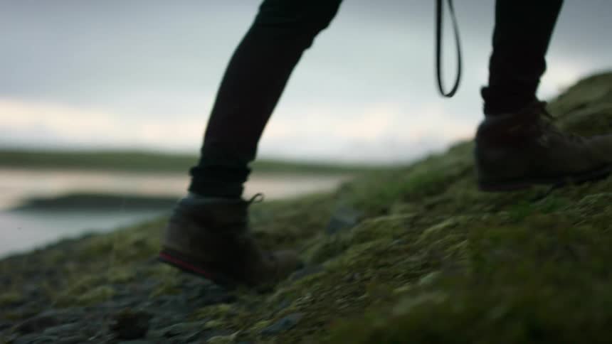 Hiker climbs a grassy hill while carrying a strap