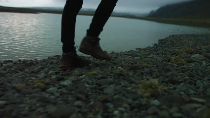 A person walking on a pebbly lakeshore on a cloudy day