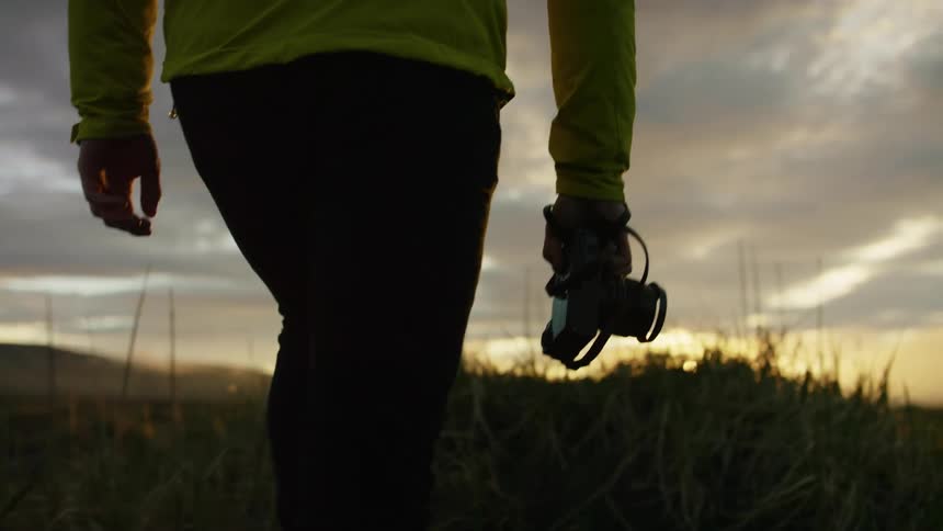 A man walks across the landscape with his camera to take a picture of the sun setting