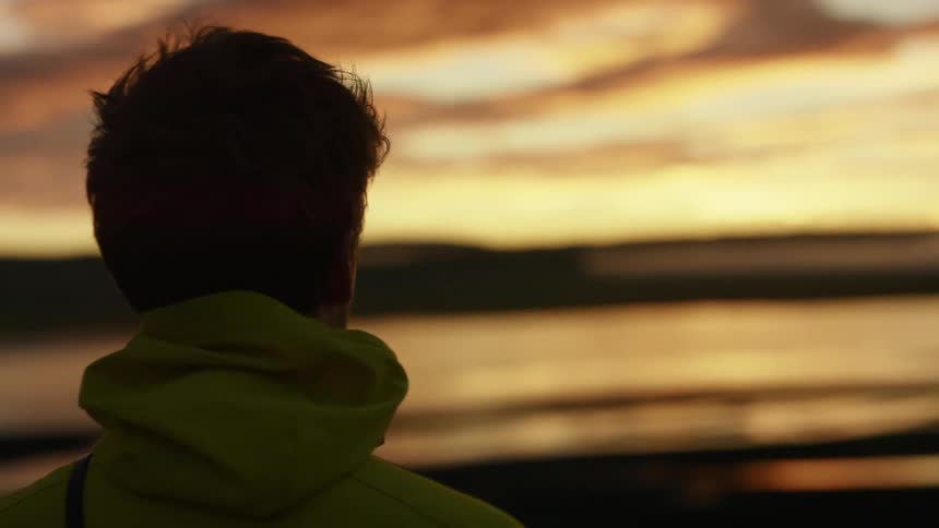 Man with a zip hooded sweatshirt watches the sea and red sky
