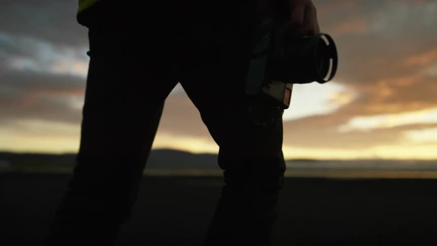 A man carrying a camera walks across the landscape