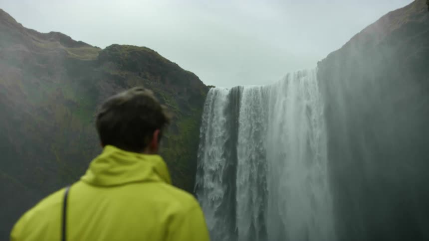 A man looks up at a waterfall on a cloudy day