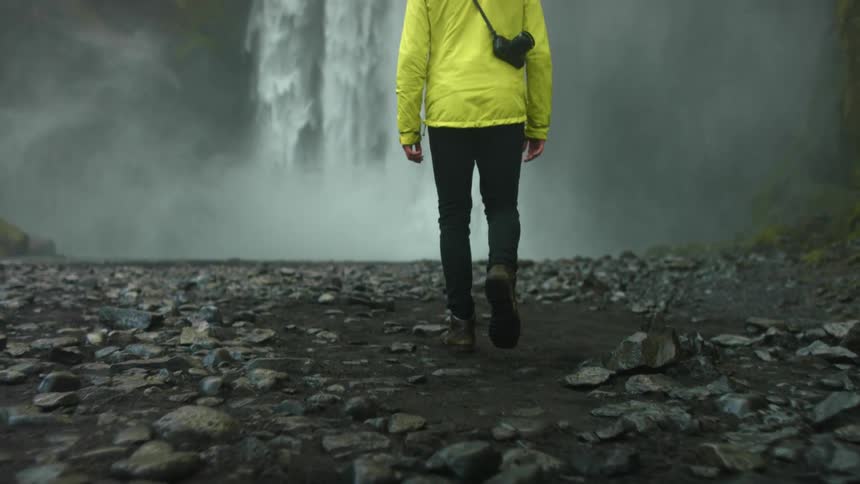 Walking across rocks towards a large flowing waterfall