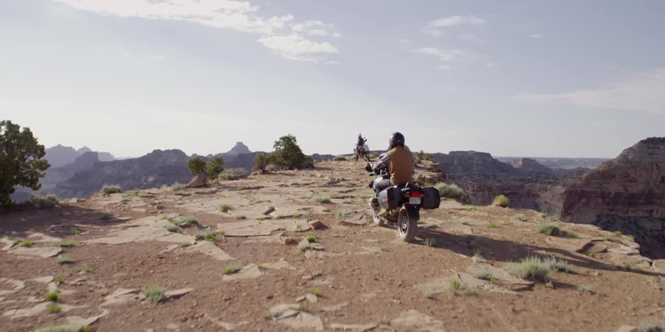 A motorcyclist rides toward the point on a cliff to another motorcyclist