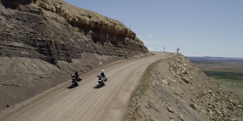 Two motorcyclists riding down a dirt road cut in a mountain