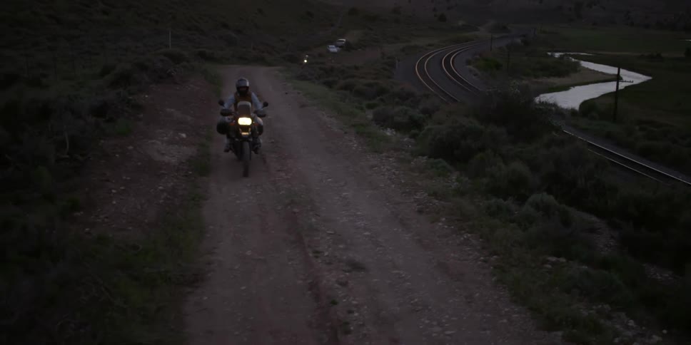Two motorcycles drive up dirt road beside a train track