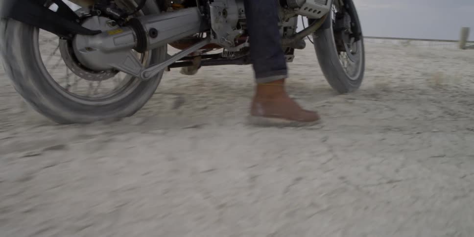 A person walks a bike through the desert before pulling away