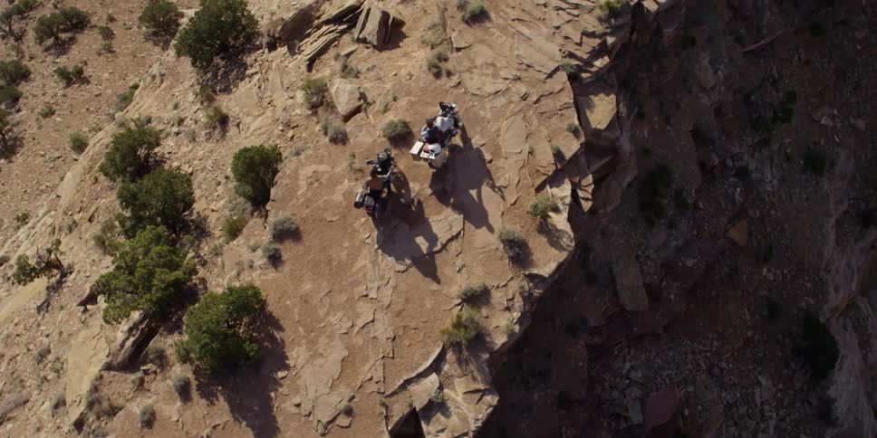 Two people on motorcycles stopped on a dirt road on a cliff