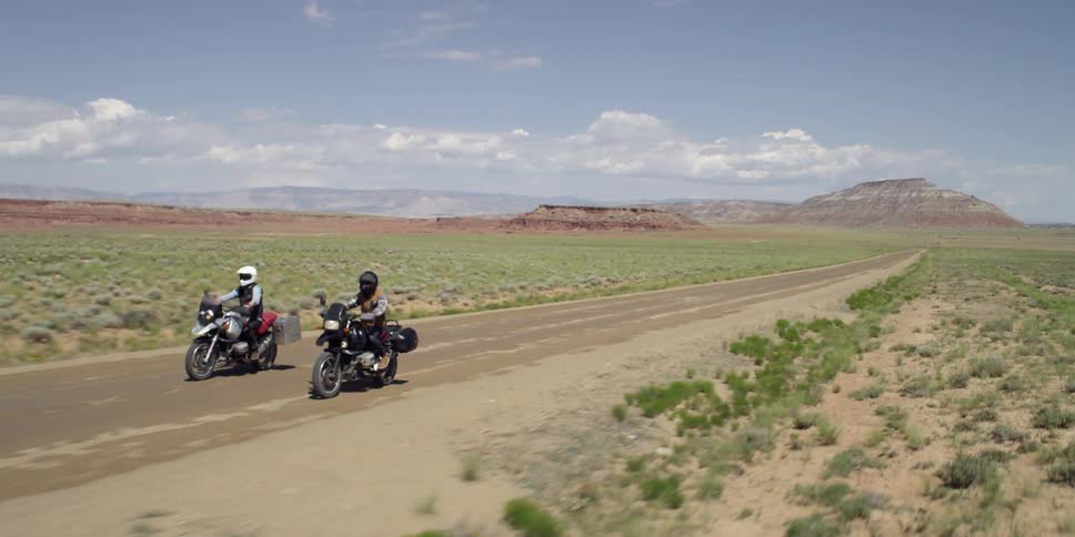 Two people on motorcycles drive down a desert road