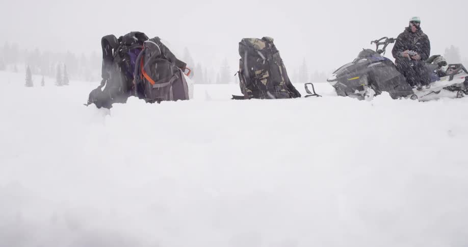 A group of backpacks sitting in snow on a snowy day