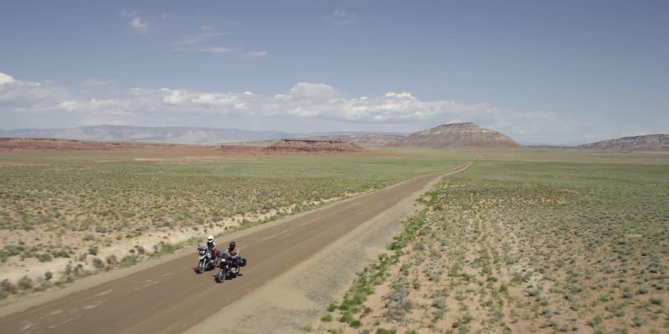 Two motorcycles drive down a road on a sunny day