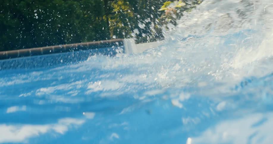 A girl wearing goggles jumps into an outdoor swimming pool on a sunny day
