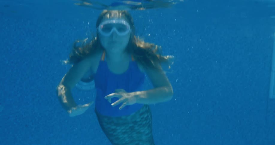 Girl swimming in a mermaid costume waving underwater