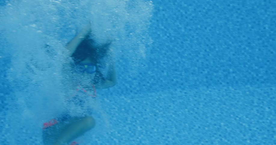 A young girl jumps into her familys swimming pool as her white dog stands nearby