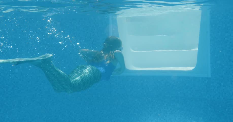 A woman swimming underwater with bubbles in a mermaid suit