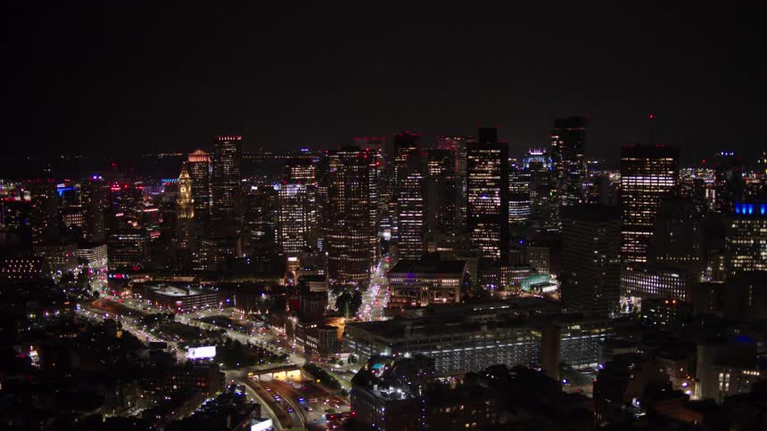 Illuminated buildings stand in the city at night while traffic travels on the city streets