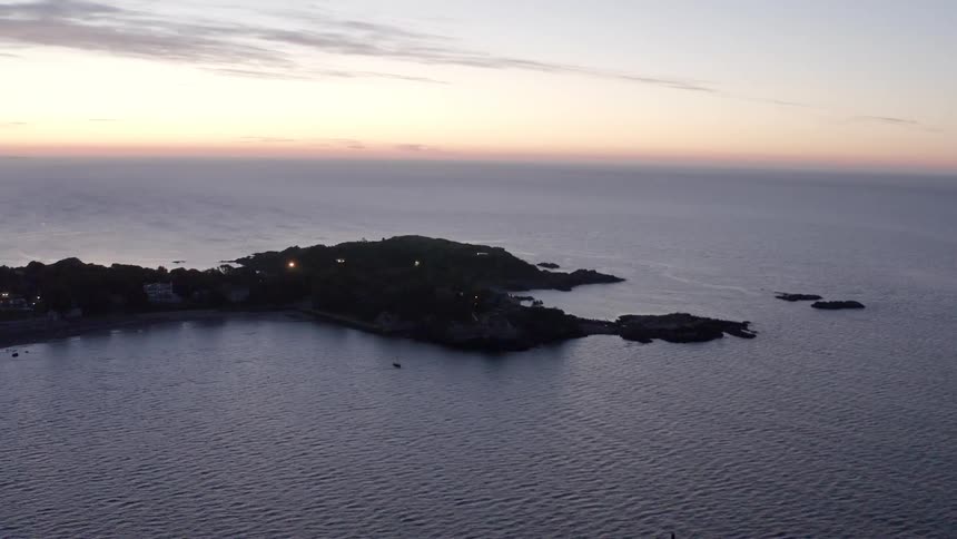 An aerial view of ocean water rippling around an island at sunrise