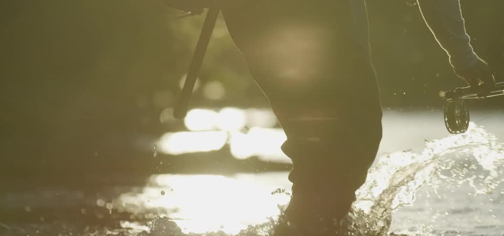 A person carrying a fishing rod into a river