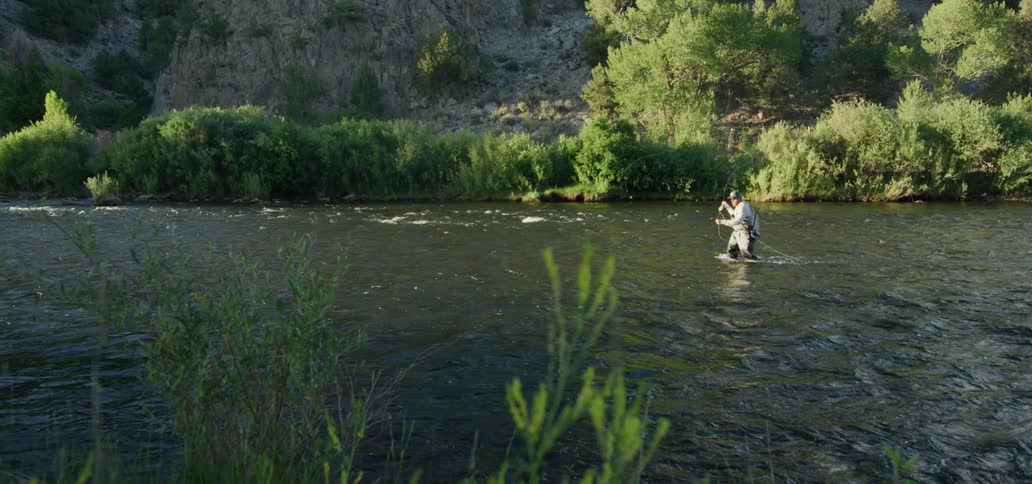 Man casts a fly fishing rod while standing in a creek