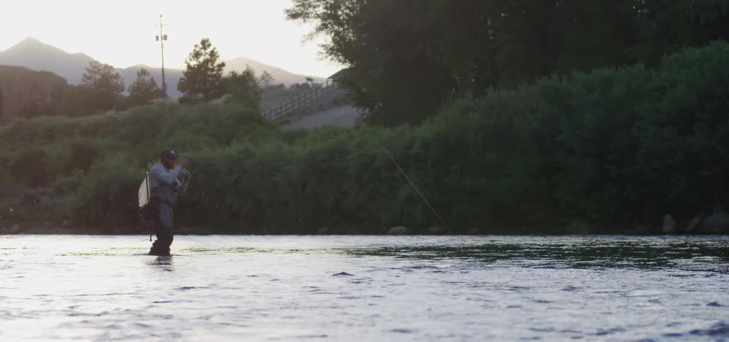 A man stands in a lake with a long fishing line out from him