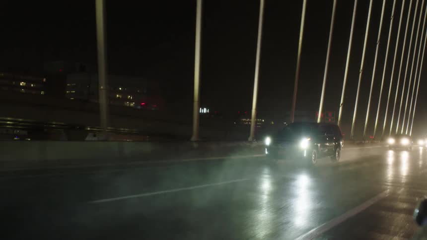 A vehicle travels along a bridge busy with traffic in a metropolis at night