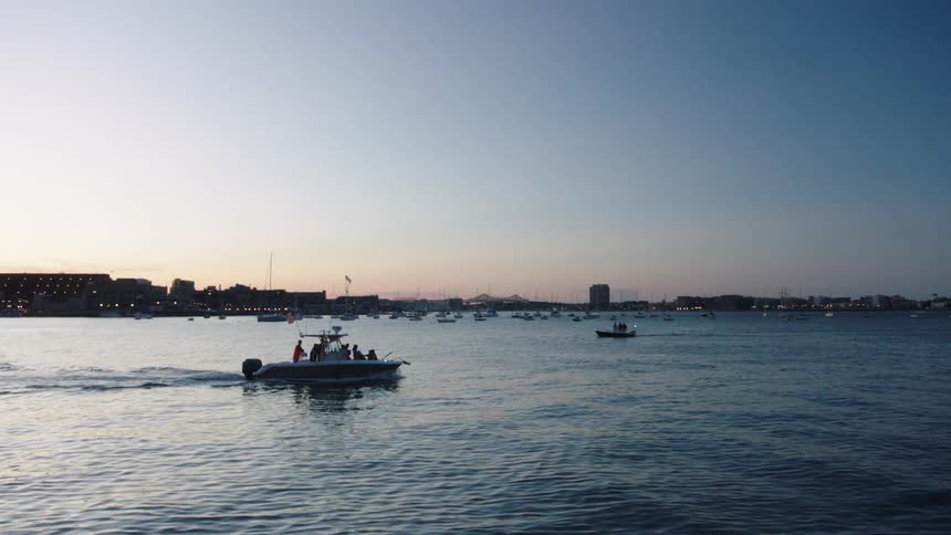 A boat carrying several people travels across a bay outside of a metropolis at sunset