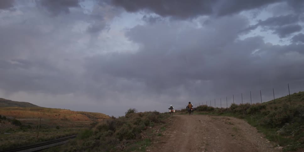 Two motorcyclists travelling along a dirt road