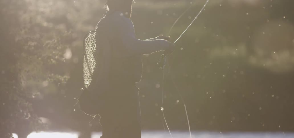 A man fishes on the side of a lake on a sunny day