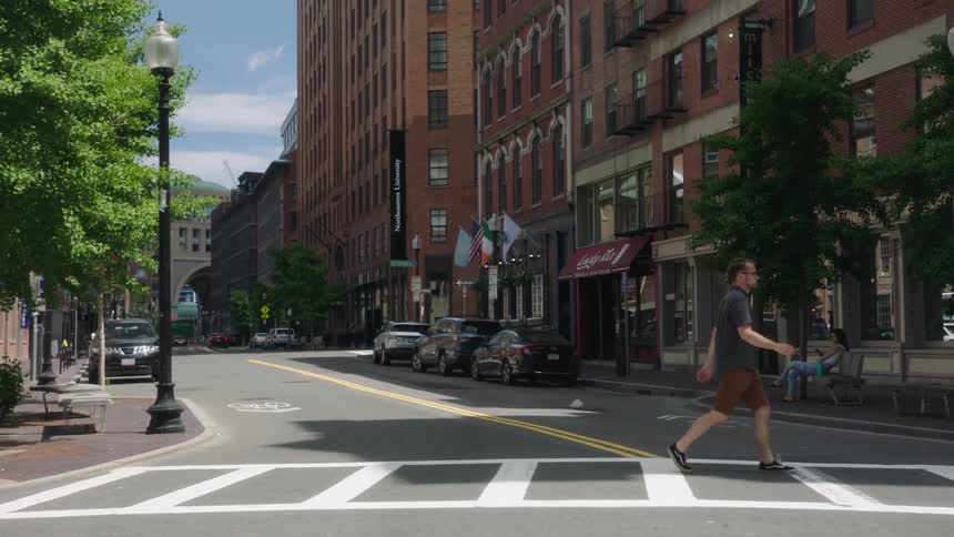 A man walks across a city street with cars parked on it