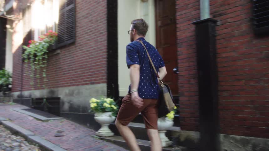 A man with glasses and a bag walking in an alley