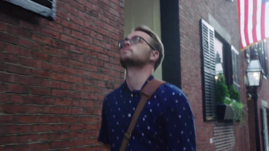 Young man in glasses with messenger bag walks down neighborhood street