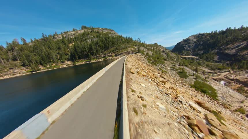 A narrow road between a lake and a mountain slope covered in stones on a sunny day