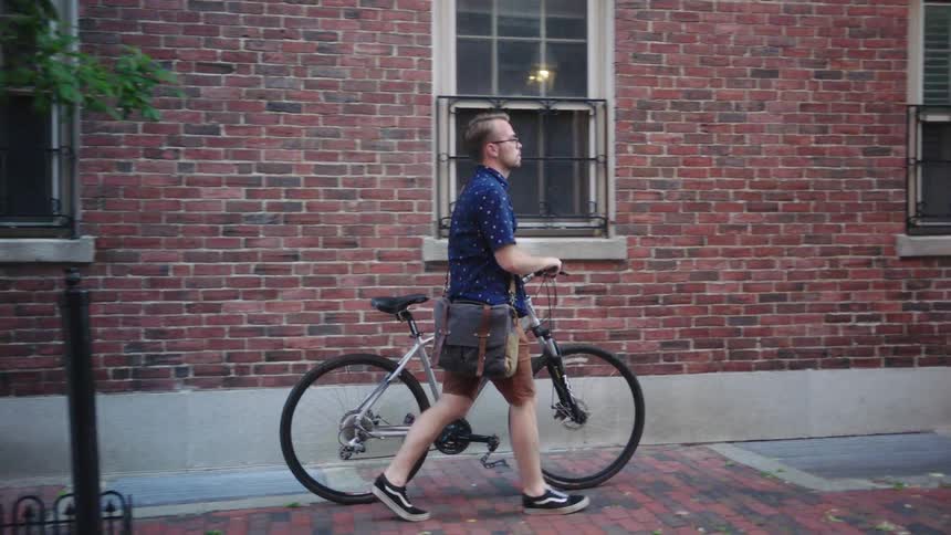 A man walks his bike down a neighborhood sidewalk