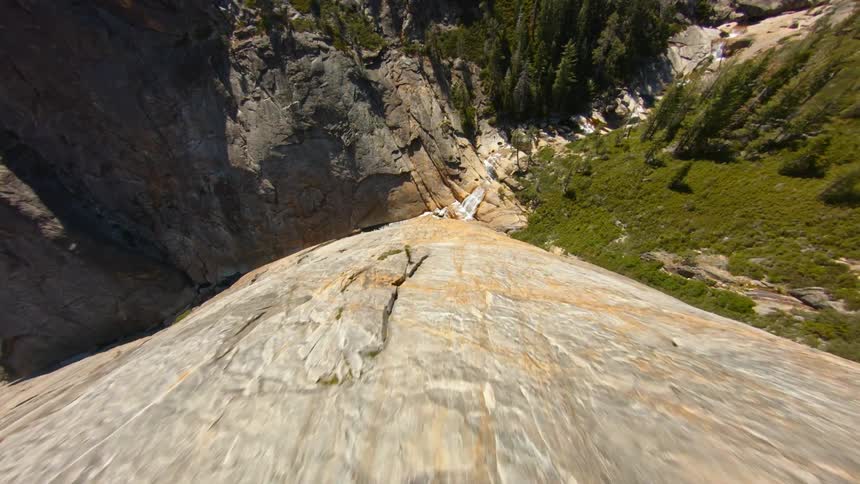 An aerial view diving down a cliff face towards a river on a sunny summer day