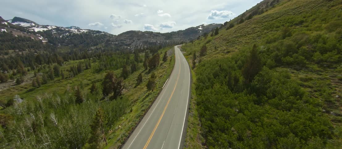 An aerial view of a road in a mountain forest in the daytime