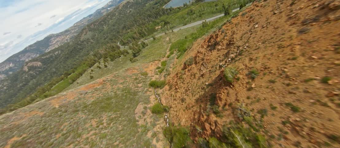 Ravine between ridges in mountain landscape with distant lake and road