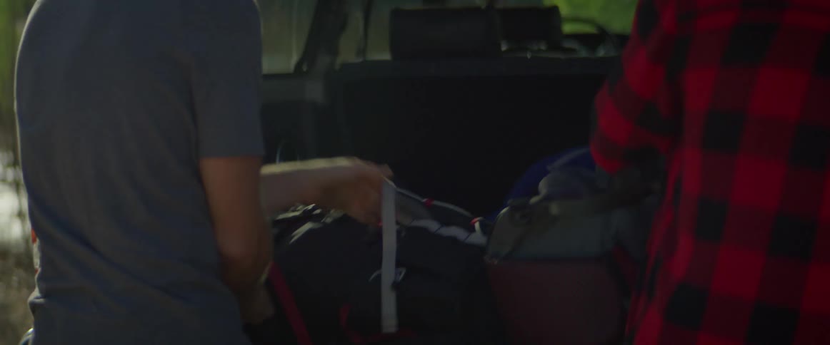 A man and woman take bags out of the back of a vehicle