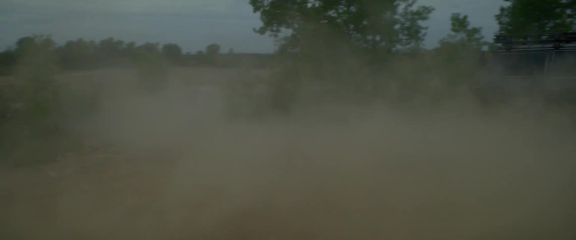 A car is driving on a dirt road during the day