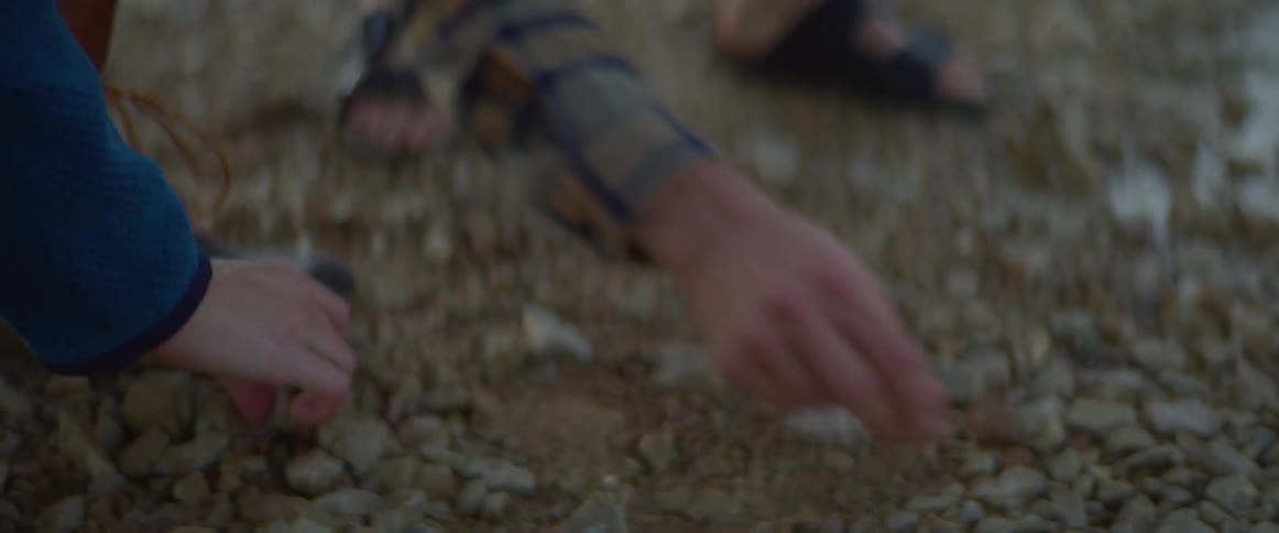 Two people stooping down and picking up rocks from the ground