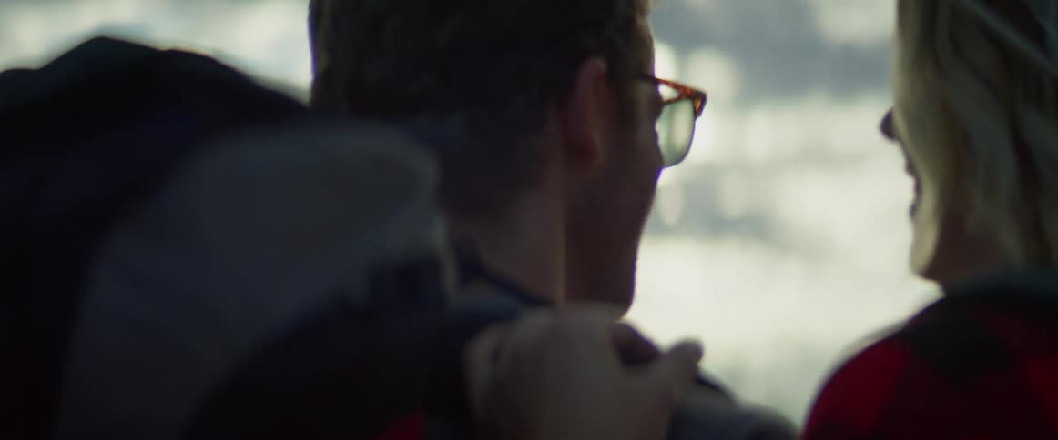 Man and woman touch affectionately while wearing backpacks outdoors