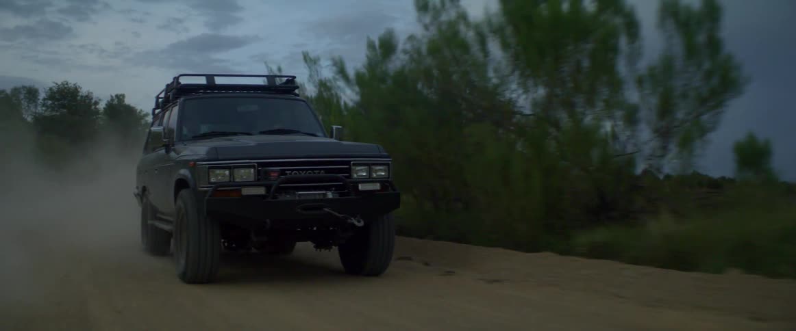 A car is driving down a dirt road in a rural area