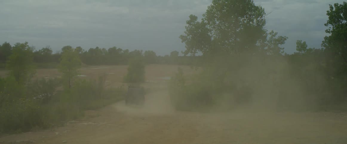 A car is driving on a dirt road in a rural area
