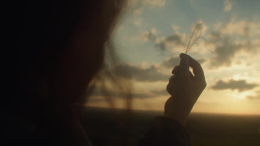 A young woman holds grass in her hand and looks at it