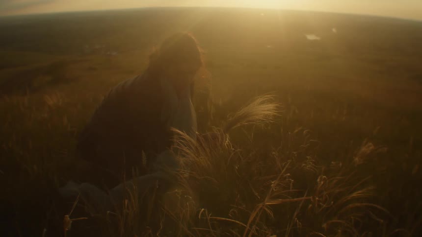 A woman is picking flowers from a field at dusk