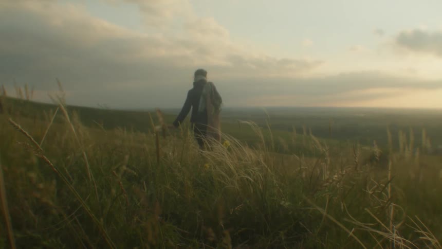 A woman carries a bag of long stalks of grass through a hilly countryside in the evening